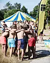 Barn och ungdomar i ring på en strandäng bredvid ett blå-gult tält och en SAU-flagga.