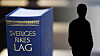 Blå bok med texten Sveriges Rikes lag bredvid en mörk siluett mot suddig bakgrund.