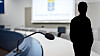 Mikrofon i en rättssal med suddig riksvapenprojicering och mörk personsiluett i förgrunden.