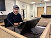 Mann med caps og briller sitter ved en datamaskin i et lyst rettsrom.