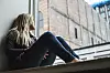 Kvinna sitter vid ett fönster och tittar ut på en byggnad på andra sidan gatan.
