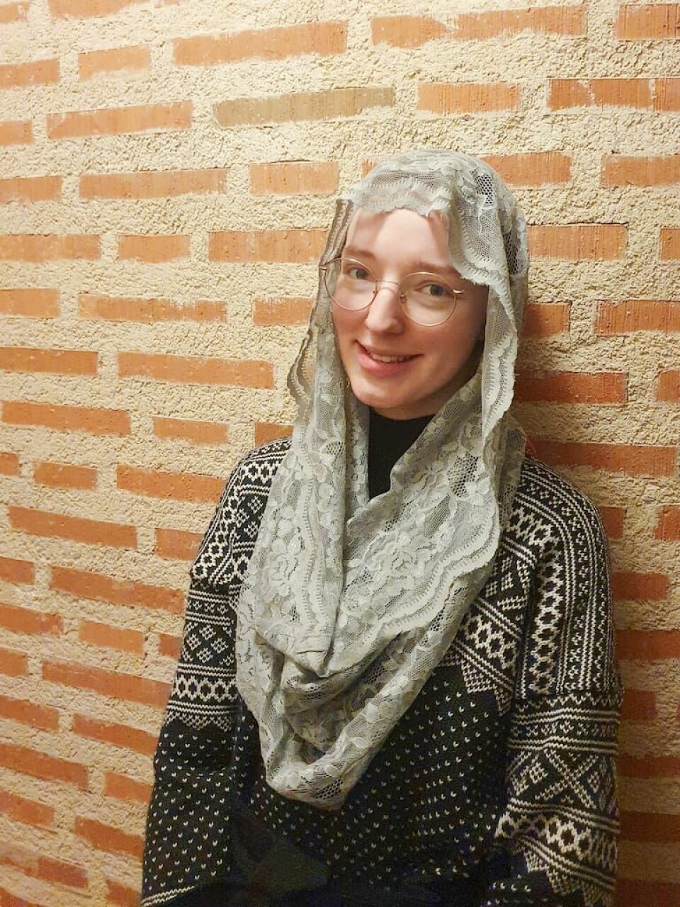 Clara Silfverswärd Dahlgren, 23 år. 23-åriga Clara Silfverswärd Dahlgren har valt att täcka sitt hår under gudstjänsten. Här syns hon mot en tegelvägg i en lång vit slöja i spets.