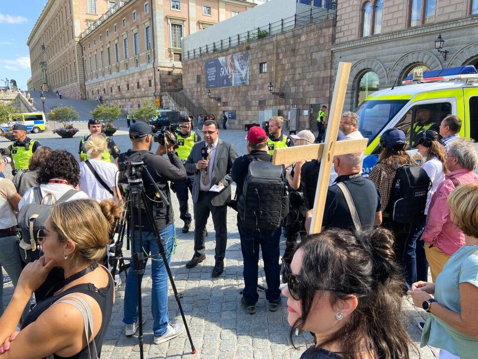 En kvinna med kors var med under koranbränningen. Två män bränner koranen på Mynttorget i centrala Stockholm.