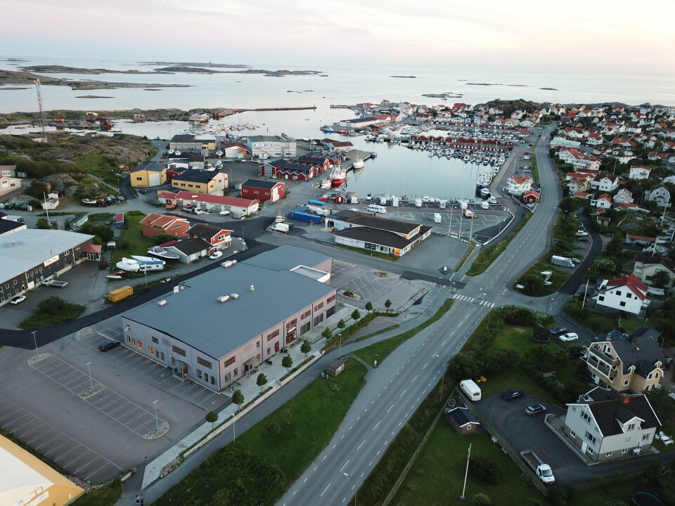 Den nya missionskyrkan på Hönö (den stora byggnaden i bildens nedre vänstra del) ligger i hamnområdet, som kan beskrivas som öns centrum. Drönarbild där man ser byggnader, vägar och havet.